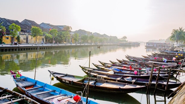 A calm river with boats docked along the shore, surrounded by traditional buildings. - Pa Pa Villa Hoi An (Da Nang)