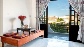 A room with a wooden bench, a vase with red flowers, and a view of a building through a window with curtains. - Pa Pa Villa Hoi An (Da Nang)
