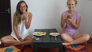 Two individuals seated on the floor, each holding a drink, with plates of food and a smartphone on a small table between them. - Pa Pa Villa Hoi An (Da Nang)