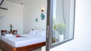A bedroom with a wooden bed, white bedding, a small table with a vase, and wall art. - Pa Pa Villa Hoi An (Da Nang)