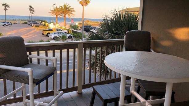 A balcony with two chairs and a small table, overlooking a parking area with cars and palm trees. - Beachside House with 2 Floors (Jacksonville Beach)