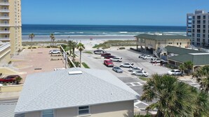 A parking lot with multiple cars, a building with a green roof, and a view of the beach and ocean. - Beachside House with 2 Floors (Jacksonville Beach)