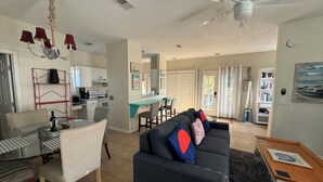 A spacious living room with a dark-colored sofa, a dining area with a glass table, and a kitchen in the background. - Beachside House with 2 Floors (Jacksonville Beach)