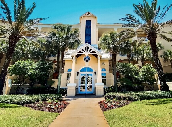 A hotel entrance with a central archway, palm trees, and a well-maintained garden.