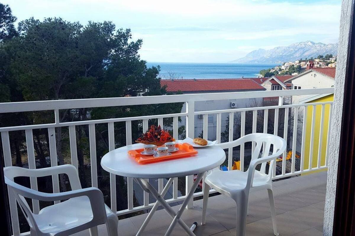 Ein Balkon mit Tisch und Stühlen, mit Blick auf die Küste, Gebäude und Berge.
