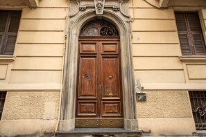 A double wooden door with a decorative arch above it, set in a building with beige walls and a window with shutters. - Cinque Terre Fancy (La Spezia)