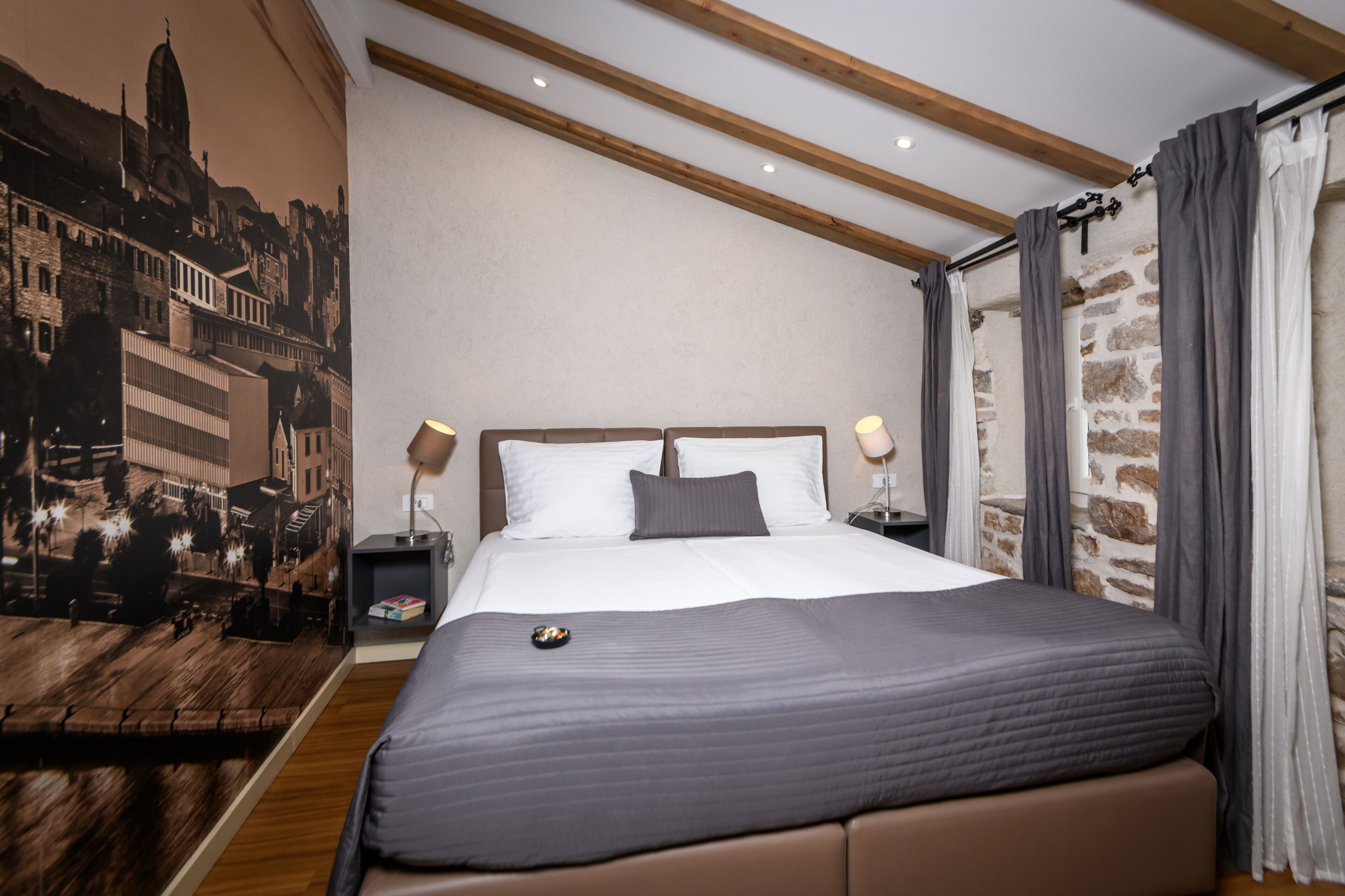 A bedroom with a large bed, wooden beams, a cityscape mural, and stone wall accents.