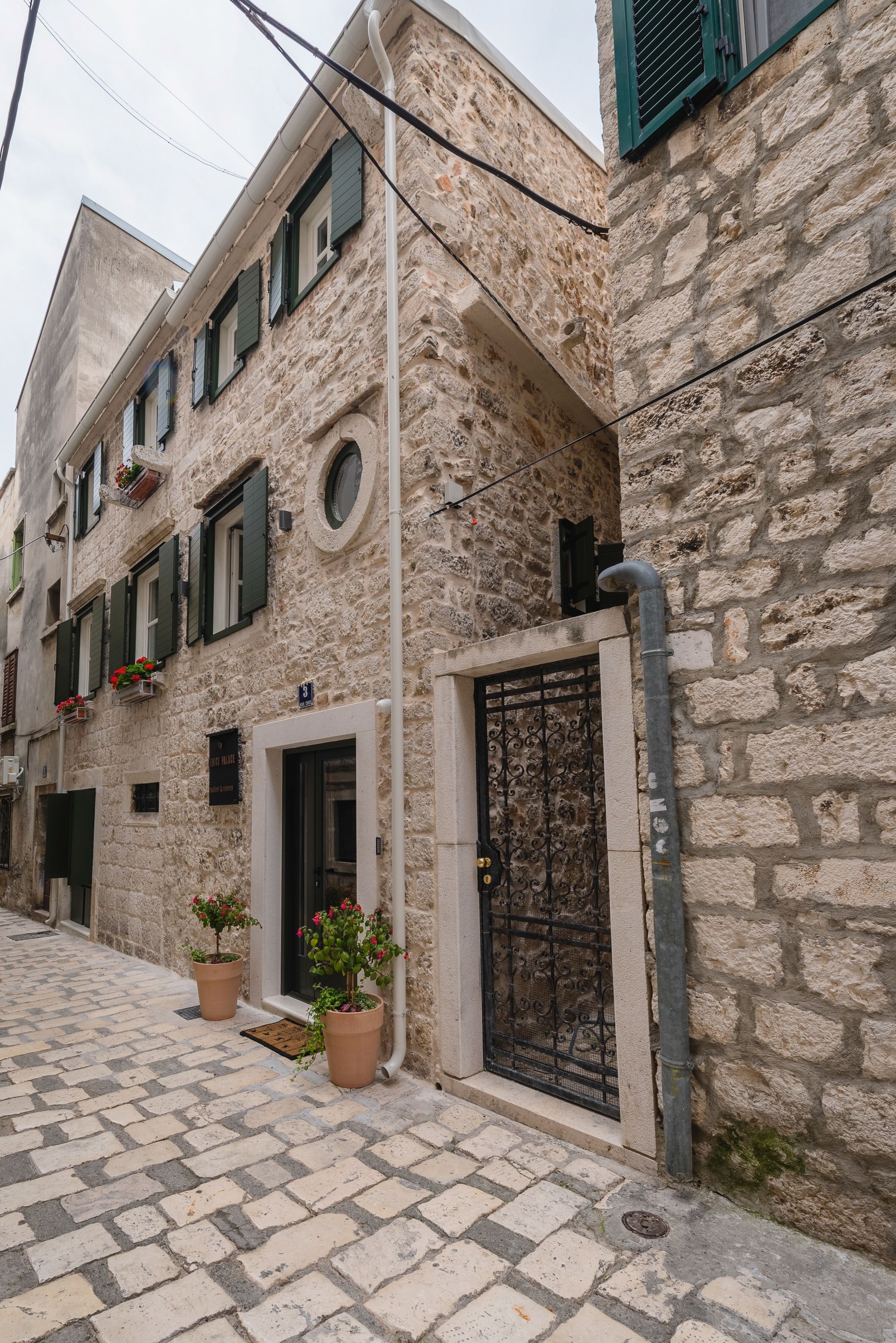 A stone building with a tiled entrance, potted plants, and a metal gate.