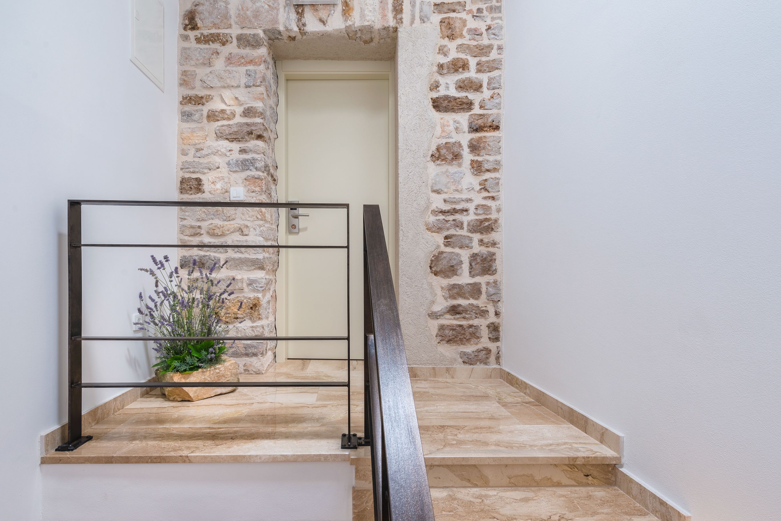 A staircase with stone walls, a metal handrail, and a potted plant.