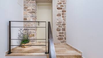 Uma escadaria com paredes de pedra, corrimão de metal e um vaso de planta.