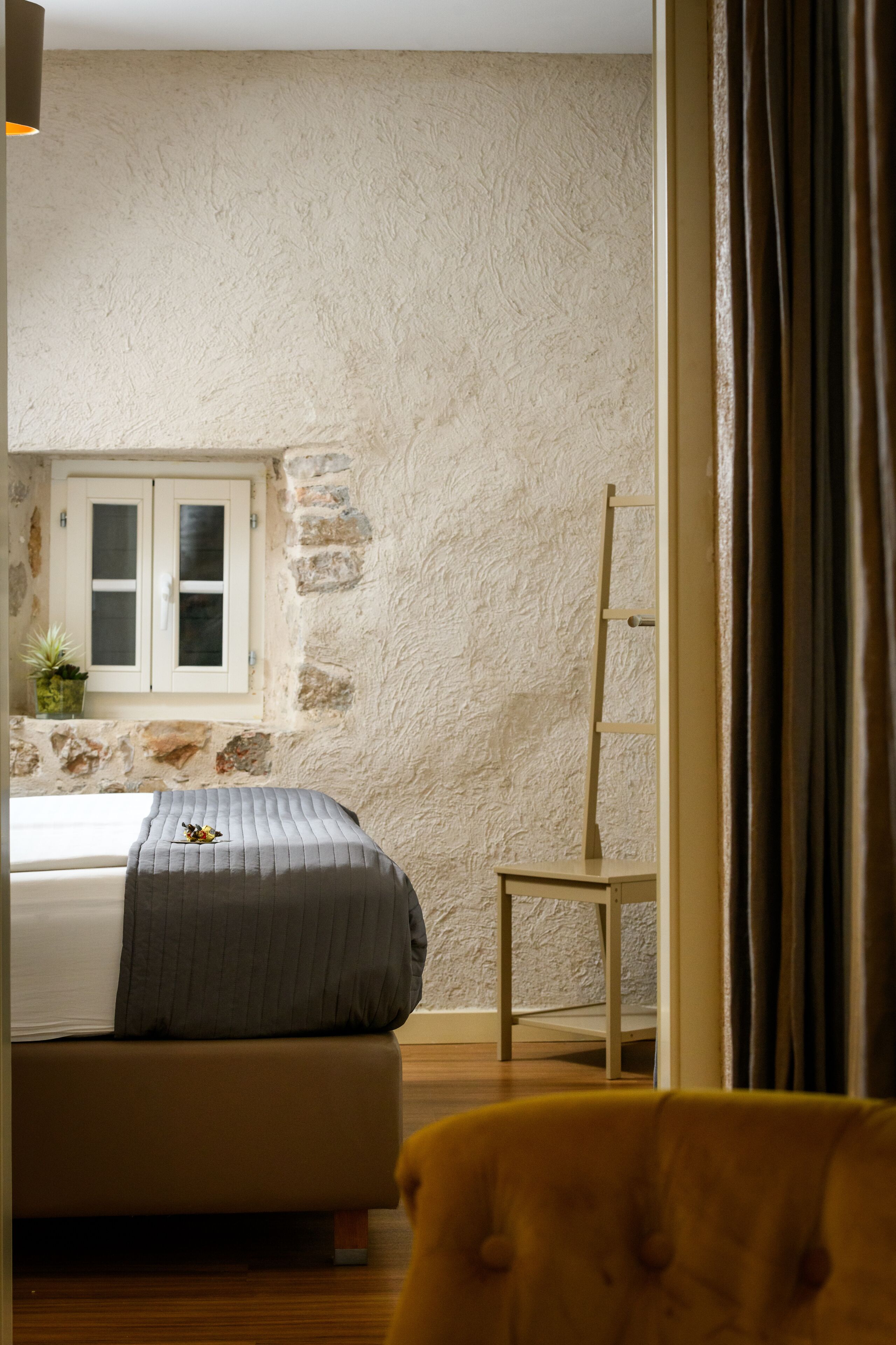 Een slaapkamer met een bed, een raam met uitzicht, een houten stoel en een plant.