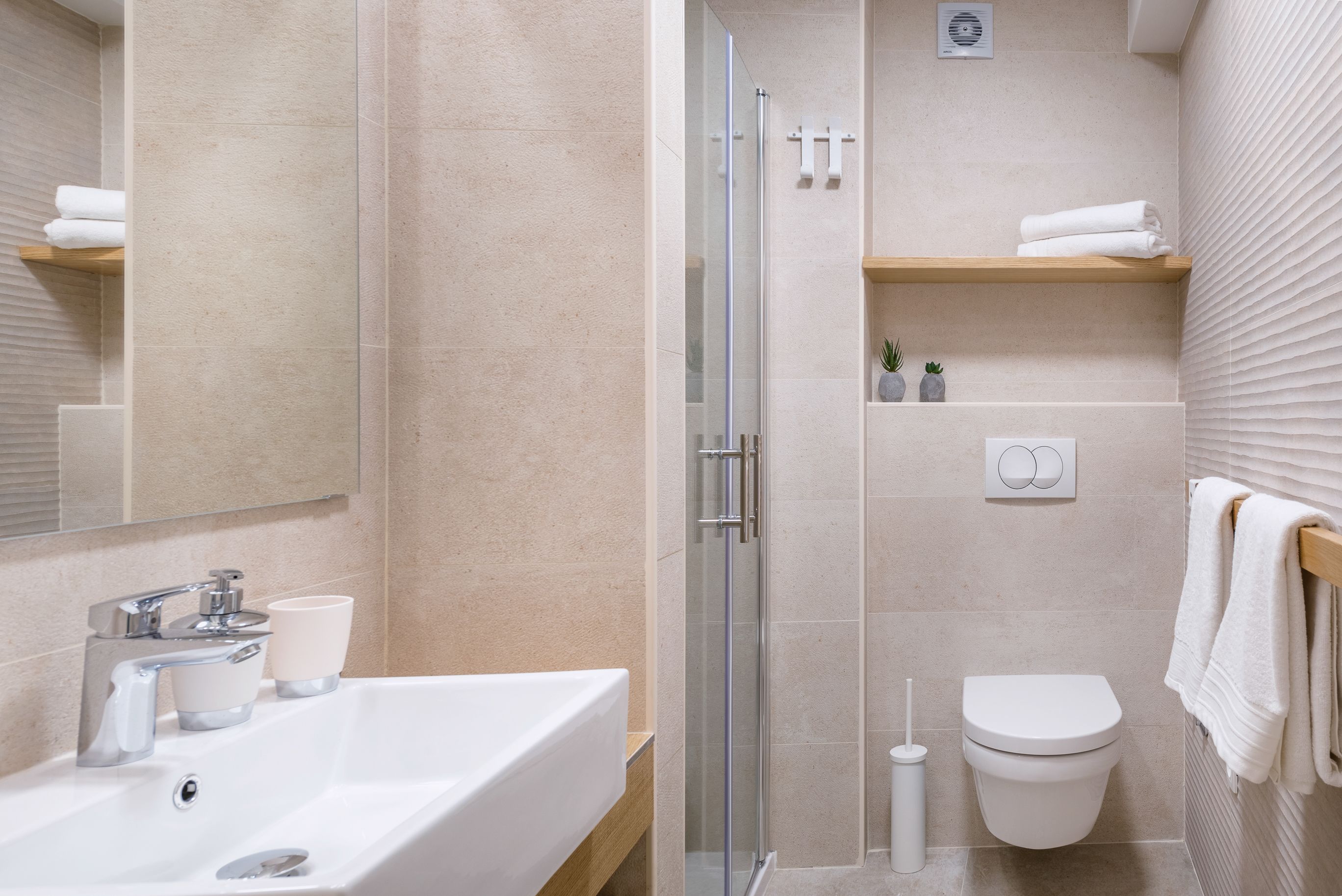 A modern bathroom with a glass-enclosed shower, a white sink with a mirror above, and a toilet with a towel rack.