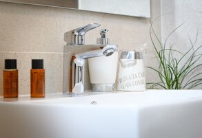 Un lavabo con rubinetto cromato, un bicchiere e due flaconi di lozione.