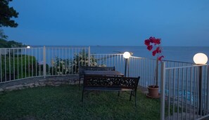A patio with a table and chairs, a potted plant, and a railing with lights.