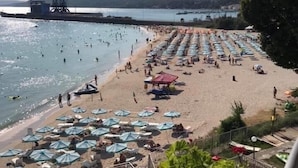 A beach with rows of umbrellas and sun loungers, a pier in the background, and a clear sky. - Hotel Helios (Balchik)