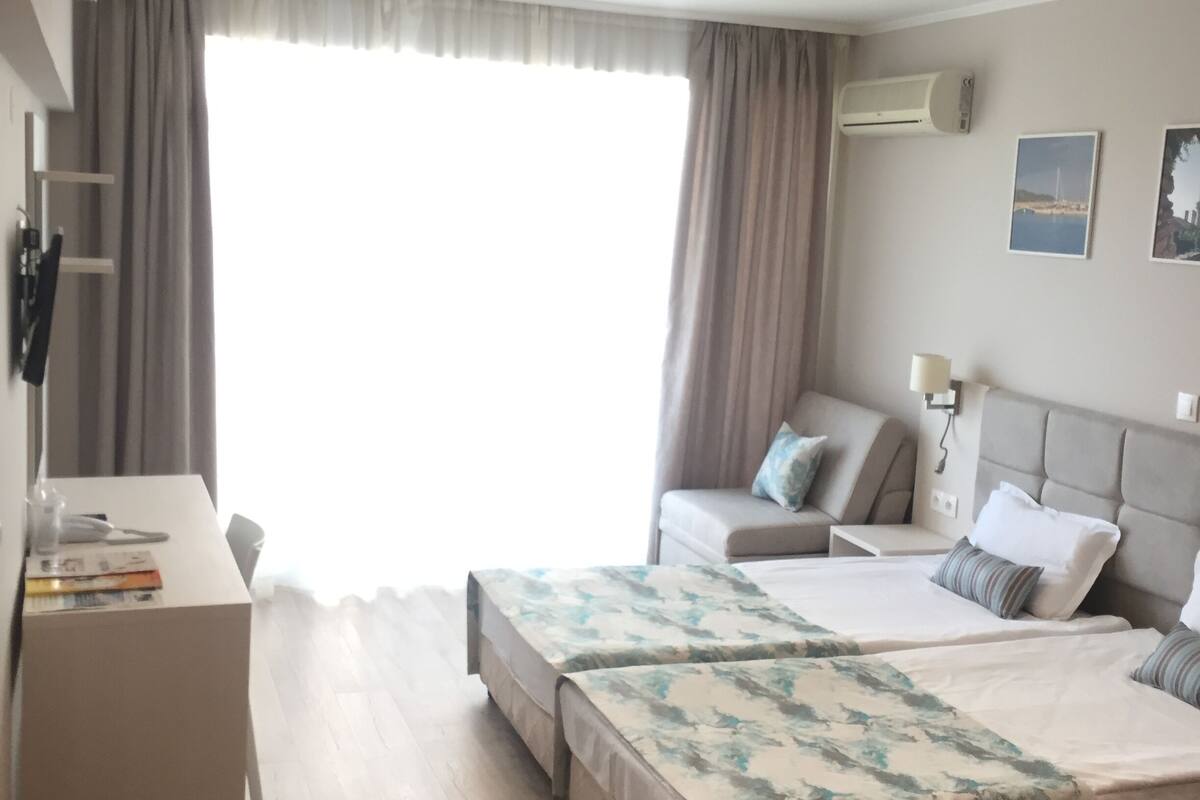 Una habitación de hotel con cama, escritorio, silla y ventana con cortinas.