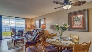 Un salón amplio con un gran ventanal que ofrece vistas panorámicas, un comedor con una mesa redonda y un ventilador de techo.