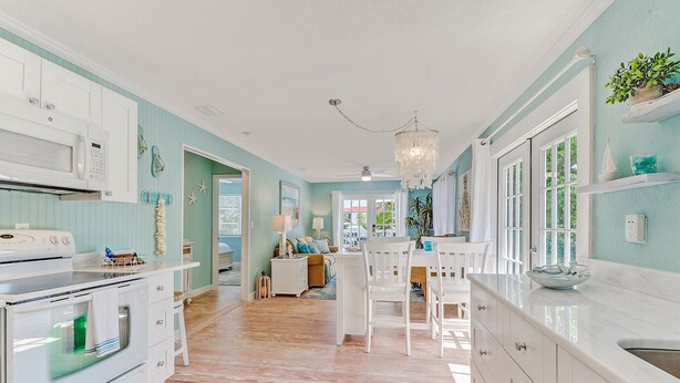 A kitchen with white cabinets, a white stove, and a dining area with white chairs and a table. - Classic Beach-Style Cottage (Naples)