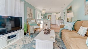 A living room with a TV, white furniture, a coffee table, and a sofa with decorative pillows. - Classic Beach-Style Cottage (Naples)