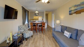 Ein Wohnzimmer mit einer Couch, einem Esstisch mit Stühlen, einem an der Wand montierten Fernseher und einem Deckenventilator.
