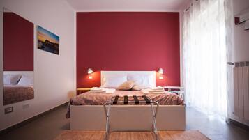 A bedroom with a bed, a nightstand, a wall-mounted picture, and a window with curtains.