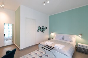 A modern bedroom with a bed, bedside tables, a chair, and a geometric-patterned rug. - Prometeo Rooms (Syracuse)