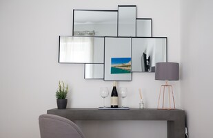 Un salón moderno con un sofá gris, una mesa de centro con una botella de vino y copas, una planta en maceta y una lámpara.