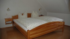Una cama de madera con una colcha blanca estampada floral en una habitación con techo inclinado y dos lámparas fijadas a la pared.