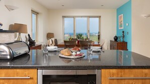 A modern kitchen with a large island, a dining area with a view, and a blue accent wall. - 5 The Vista, Newquay -  Walk to Beach - Free Parking & WiFi - Sea & Beach Views (Newquay)