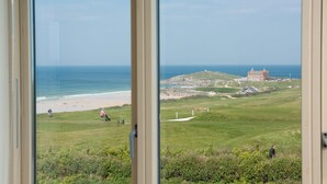 A coastal view with a beach, grassy area, and a large building in the distance. - 5 The Vista, Newquay -  Walk to Beach - Free Parking & WiFi - Sea & Beach Views (Newquay)