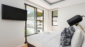 Une chambre moderne avec un grand lit, un téléviseur à écran plat et une vue sur les immeubles par une grande fenêtre.