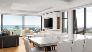 Un salon moderne avec une grande table à manger, des canapés blancs et un téléviseur à écran plat fixé au mur.