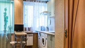 Una cocina compacta con lavadora, una mesita con sillas, un radiador y una ventana con cortinas.