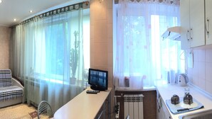 A cozy living area with a sofa, a flat-screen TV, a small table with books, and a kitchen area with a kettle and teapot. - Studio in the center near the Botanical Garden (Pechers'kyi district)