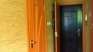A hallway with two wooden doors, one open and one closed, leading to a dark-colored door with a welcome mat. - Studio in the center near the Botanical Garden (Pechers'kyi district)