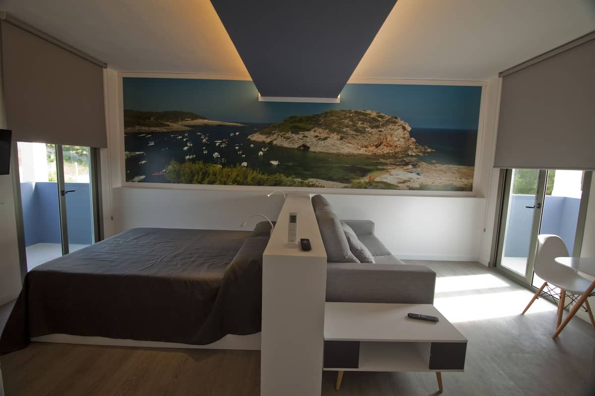 Un dormitorio moderno con una cama grande, un escritorio empotrado, vistas al mar y un balcón con una silla.