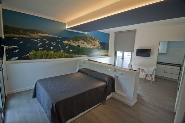 Une chambre moderne équipée d’un lit, d’un bureau et offrant une vue sur la mer par une fenêtre.