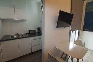 A compact kitchen with a sink, toaster, and coffee maker. A flat-screen TV is mounted on the wall.