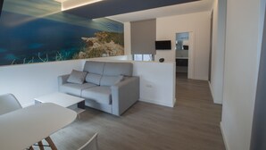 A modern living room with a grey sofa, a white coffee table, and a painting of a coastal scene. - Hostal Sa Vinya Suites (Sant Joan de Labritja)