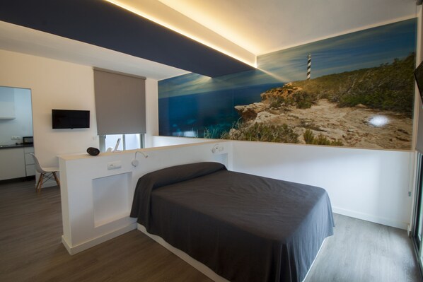 A modern bedroom with a bed, a desk, and a large mural of a lighthouse on the wall.