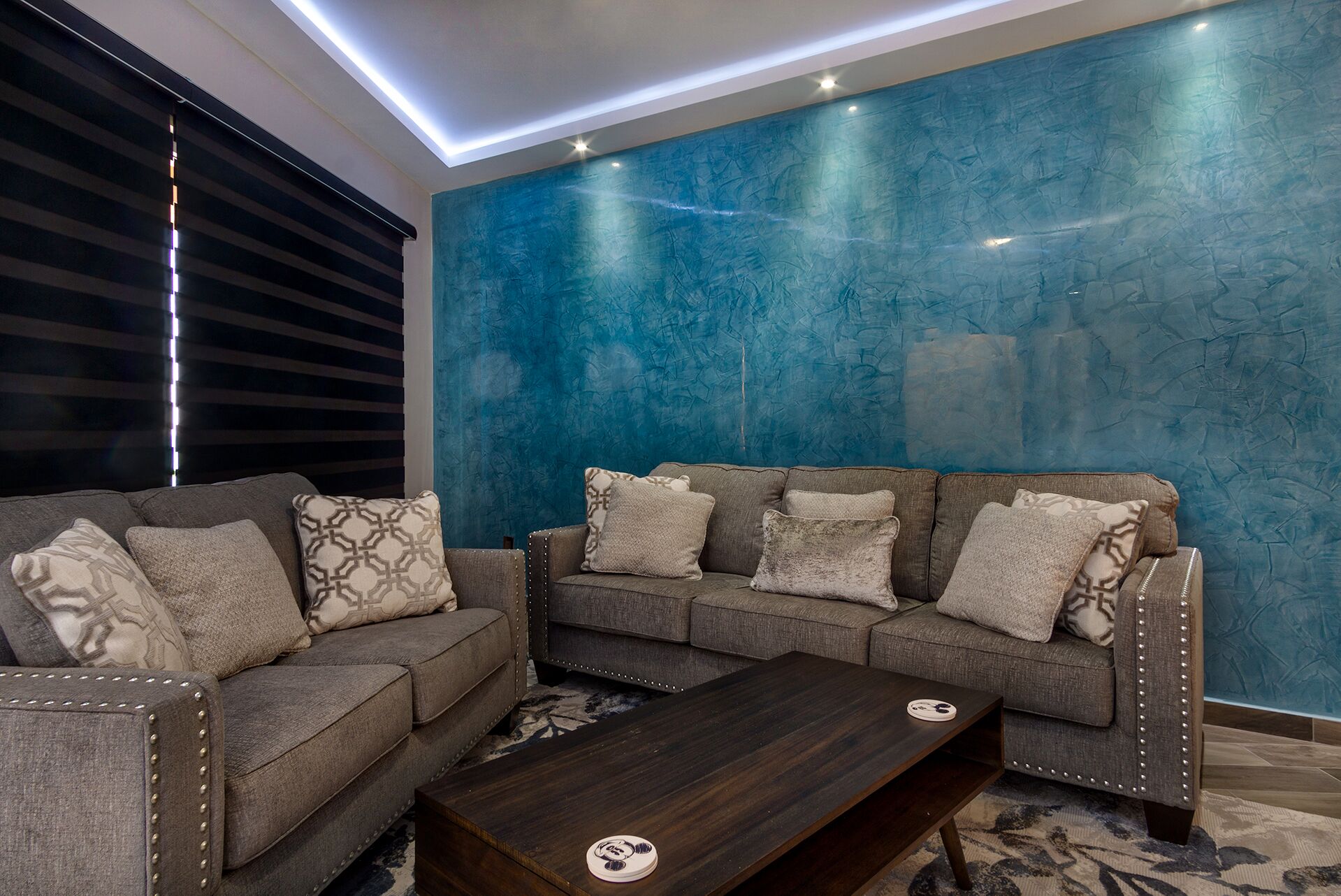 Un salon moderne avec un canapé d’angle, une table basse et un mur bleu à texture.