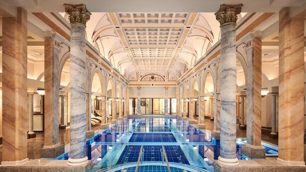 Una amplia piscina interior con columnas de mármol y techo alto.