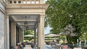 Un patio al aire libre con mobiliario de mimbre, una fuente y un gran árbol con flores blancas.