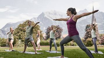 Een groep mensen doet yoga op matten in een openlucht omgeving, met een berg op de achtergrond.