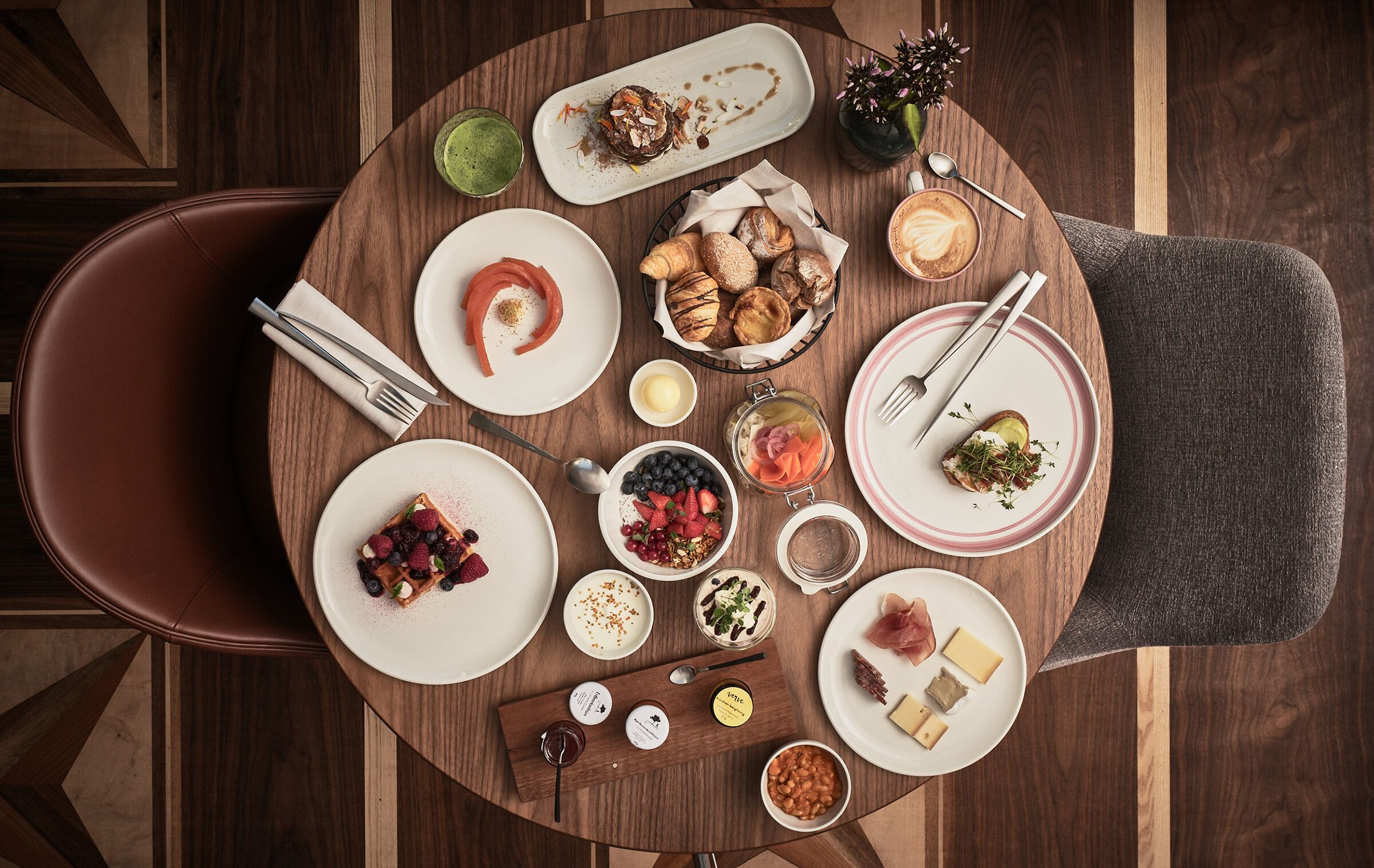 Une table ronde, dressée pour un repas, sur laquelle on a disposé divers plats, notamment des pâtisseries, des fruits et des fromages.