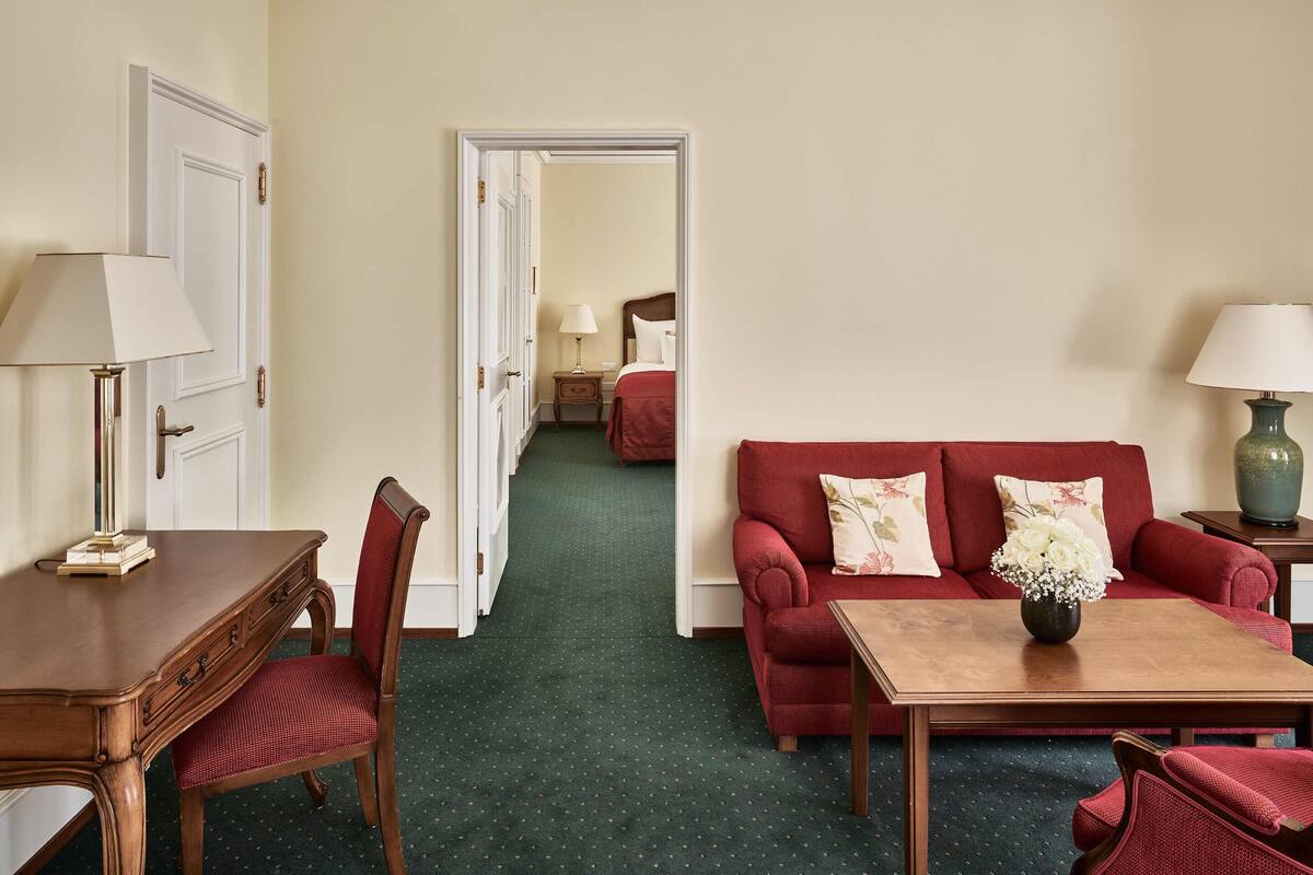Ett hotellrum med ett skrivbord i trä, en röd soffa, ett soffbord och en lampa.