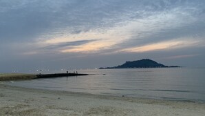 Una playa con un mar tranquilo, una montaña a lo lejos y un muelle con gente.