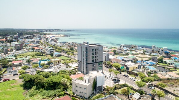A coastal town with a prominent hotel featuring a modern design, surrounded by residential buildings and lush greenery. - Lemain hotel (Jeju City)