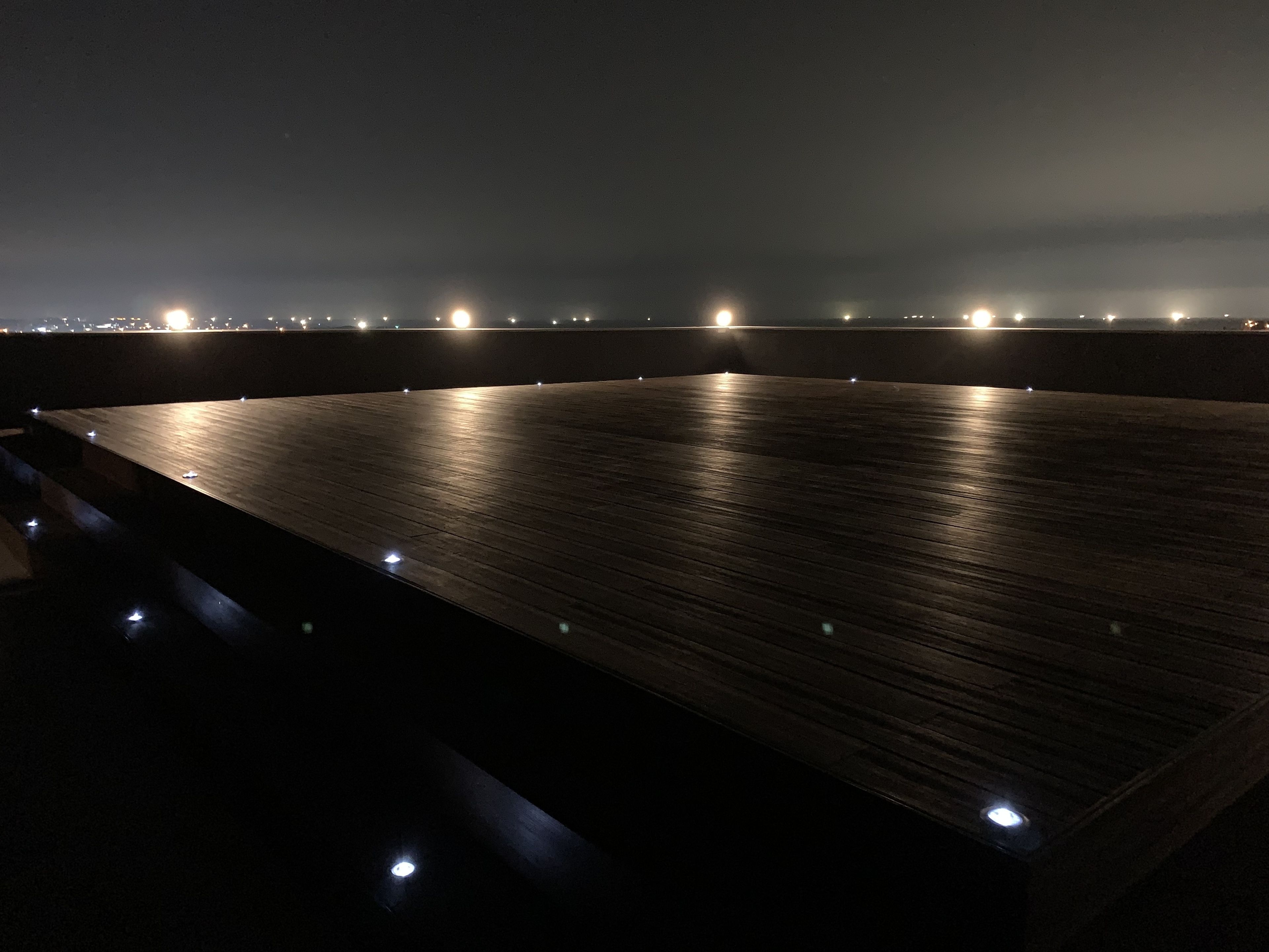 Amplia terraza de madera oscura con vista al horizonte urbano nocturno.