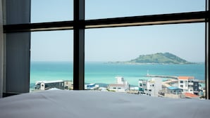 Habitación de hotel con un ventanal que da a la costa, incluyendo una pequeña isla y edificios a lo largo de la orilla.